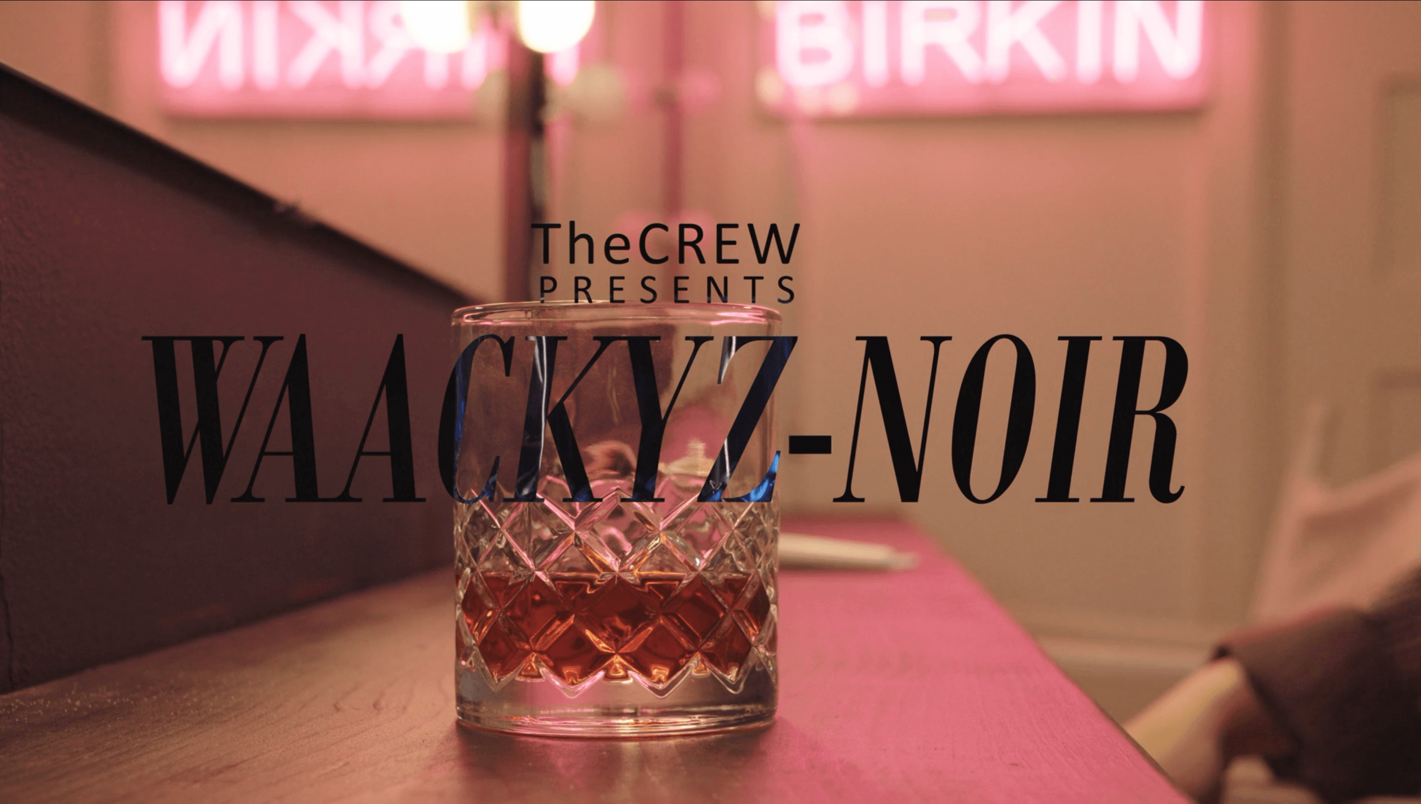 A whisky glass on a bar counter in a pink-lit lounge with the WAACKYZ-NOIR title and “The CREW presents” caption.